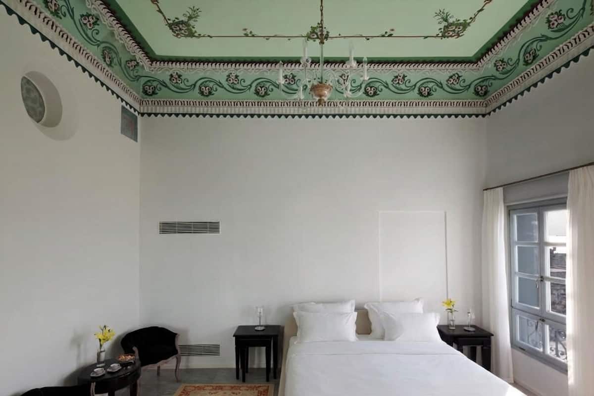 A bedroom with a large bed, a chandelier, a window, and a decorative ceiling.