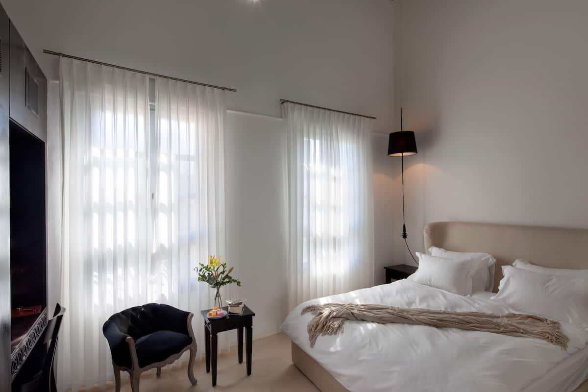 A hotel room with a bed, a chair, a small table with a vase of flowers, and a TV.