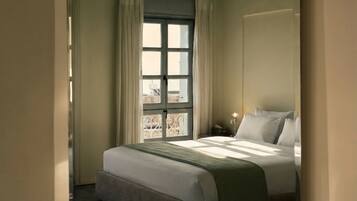 A bedroom with a bed, curtains, a window, and a wall-mounted light fixture.