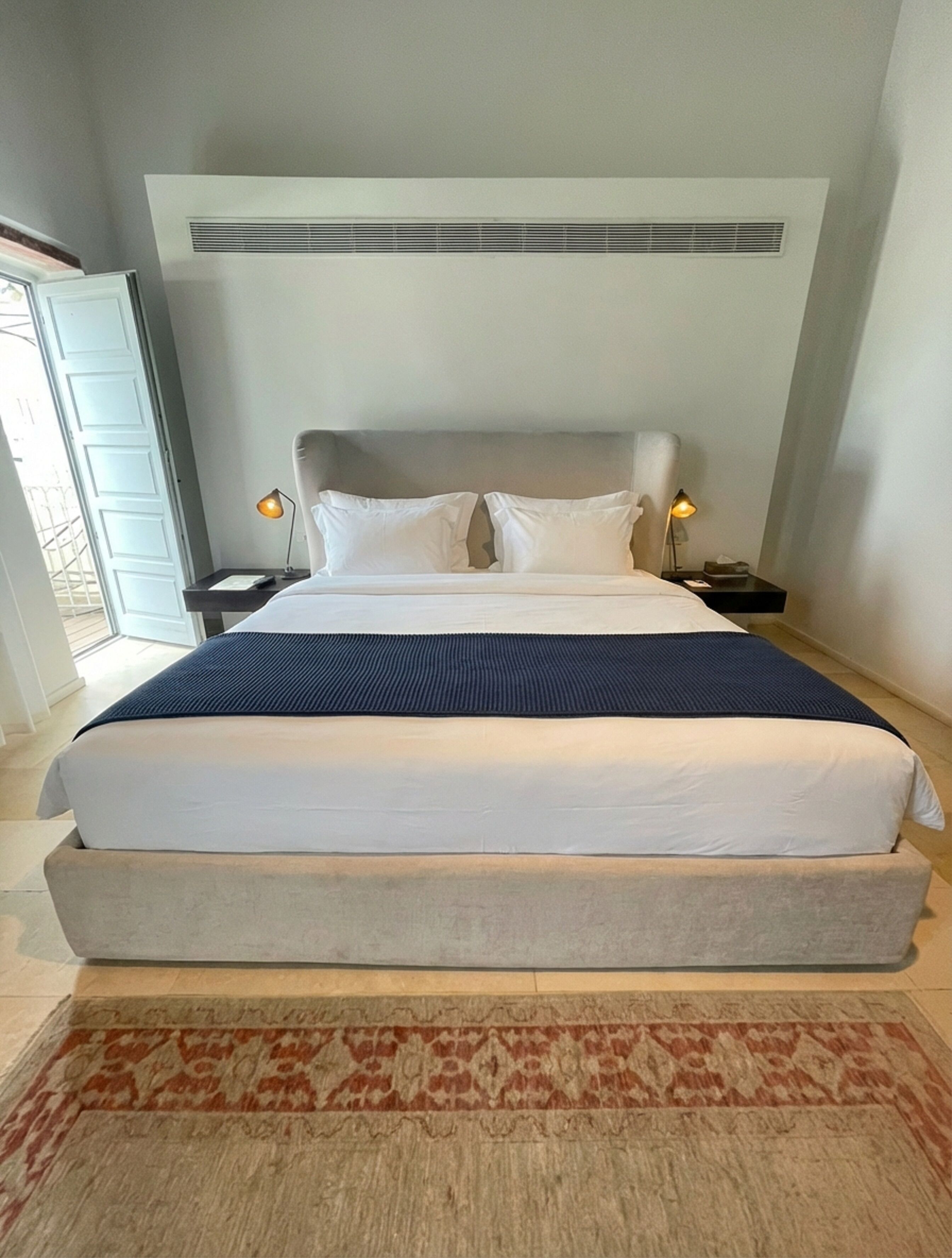 A large bed with a headboard, two bedside lamps, and a patterned rug.