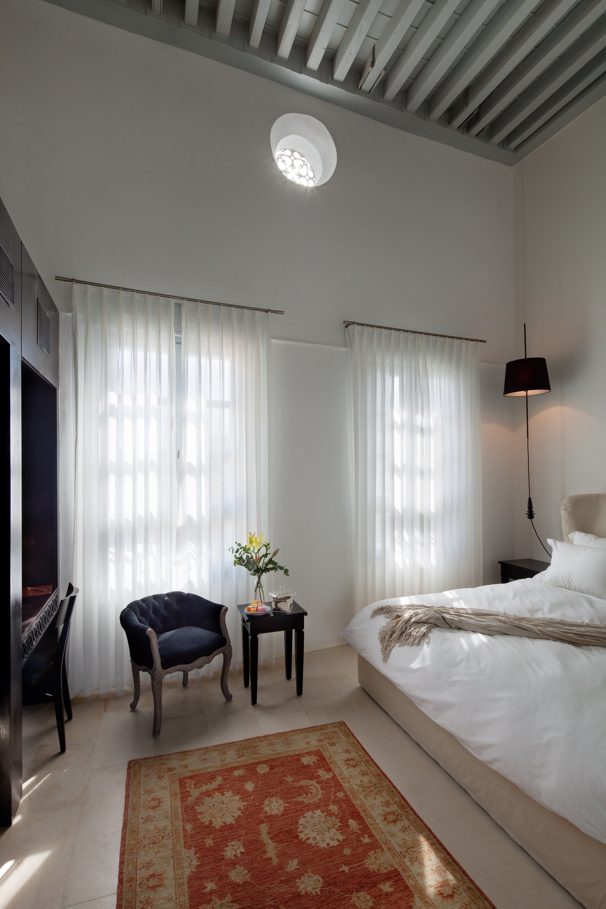 A bedroom with a bed, a chair, a small table with a vase, and a lamp.