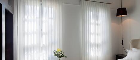 Un dormitorio con una cama, una silla, una mesita de noche con un florero y una lámpara.