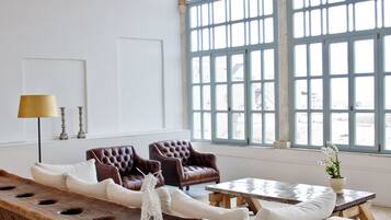 A spacious living room with a large sofa, two armchairs, a wooden coffee table, and a chandelier.