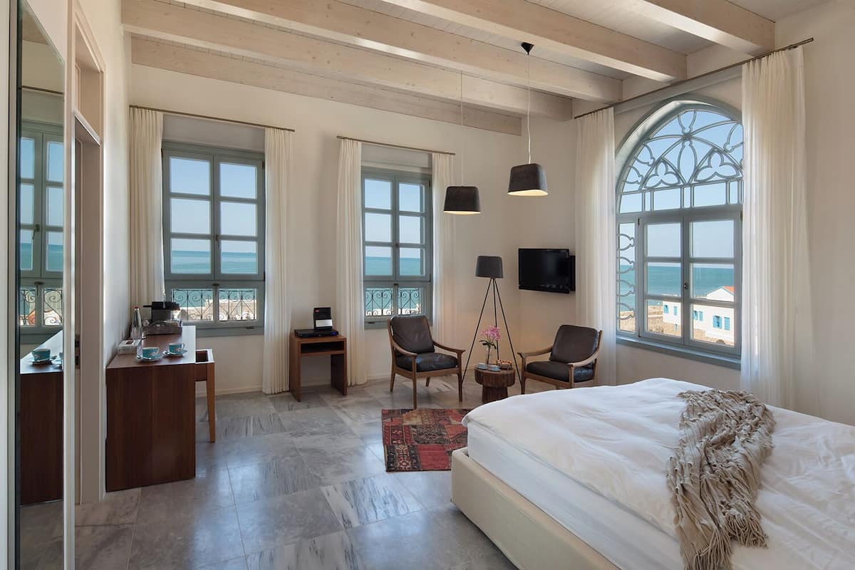 A modern hotel room with a large bed, two chairs, a desk, and a TV.