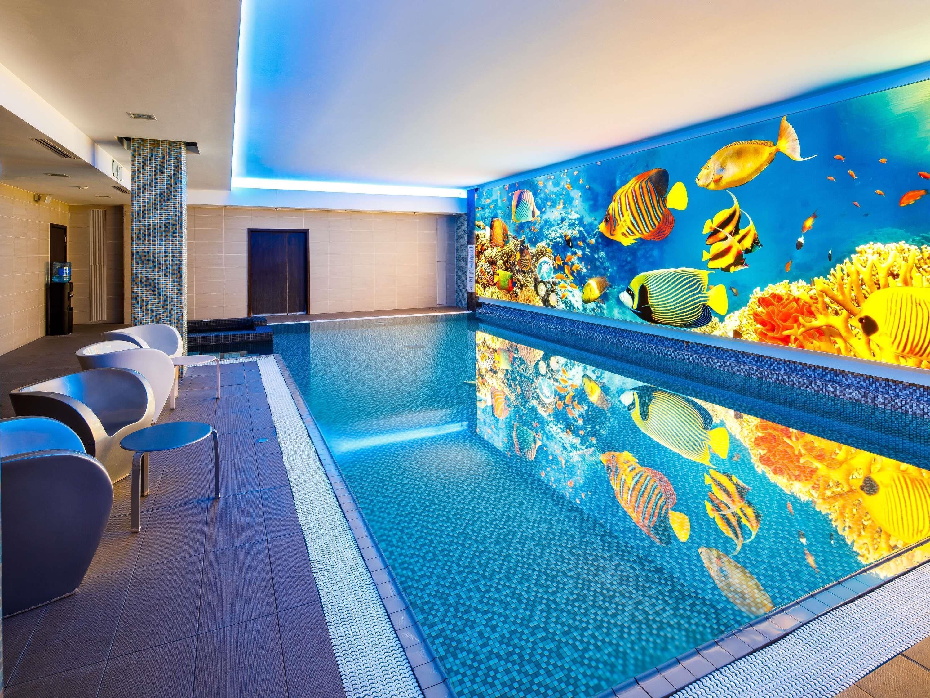 Ein Schwimmbecken mit gefliestem Boden, einer Wandmalerei mit Fischen und moderner Sitzgelegenheit am Pool.