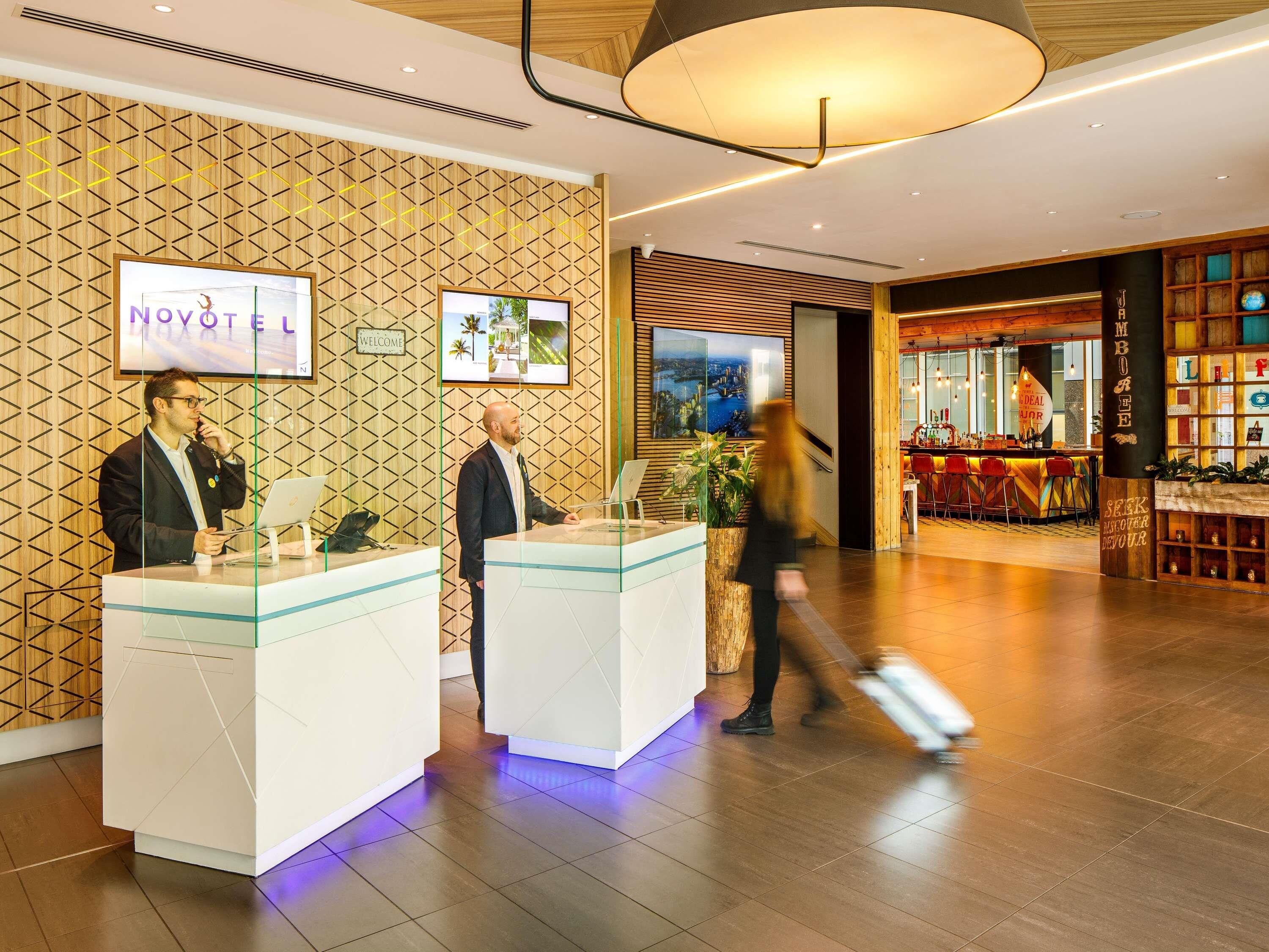 A reception area with a modern design, featuring a wooden wall pattern, a reception desk, and a bar area with stools.