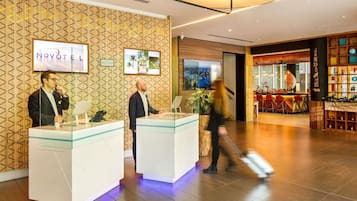 A reception area with a modern design, featuring a wooden wall pattern, a reception desk, and a bar area with stools.