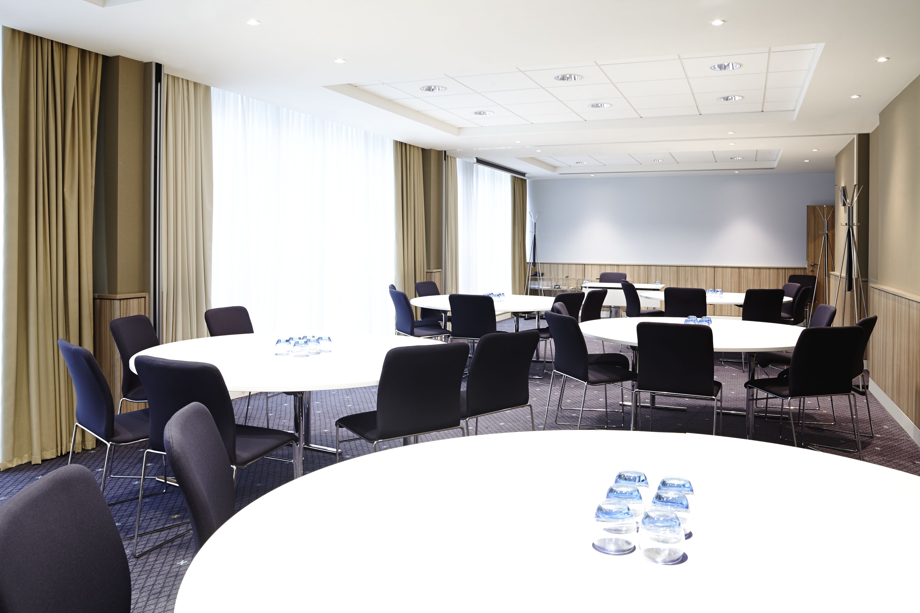 Ein Konferenzraum mit einem großen, ovalen Tisch, schwarzen Stühlen und einer Projektionsleinwand.