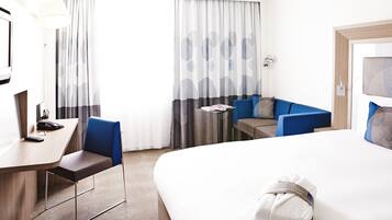 Ein Hotelzimmer mit Bett, Schreibtisch, Stuhl, kleinem Tisch und einer Couch.