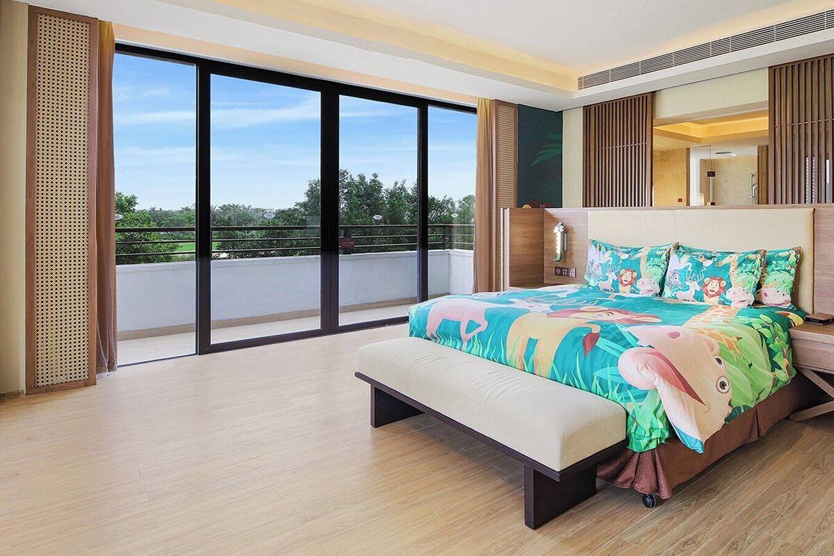 A modern bedroom with a large bed, a bench, a TV, and a balcony with a view.