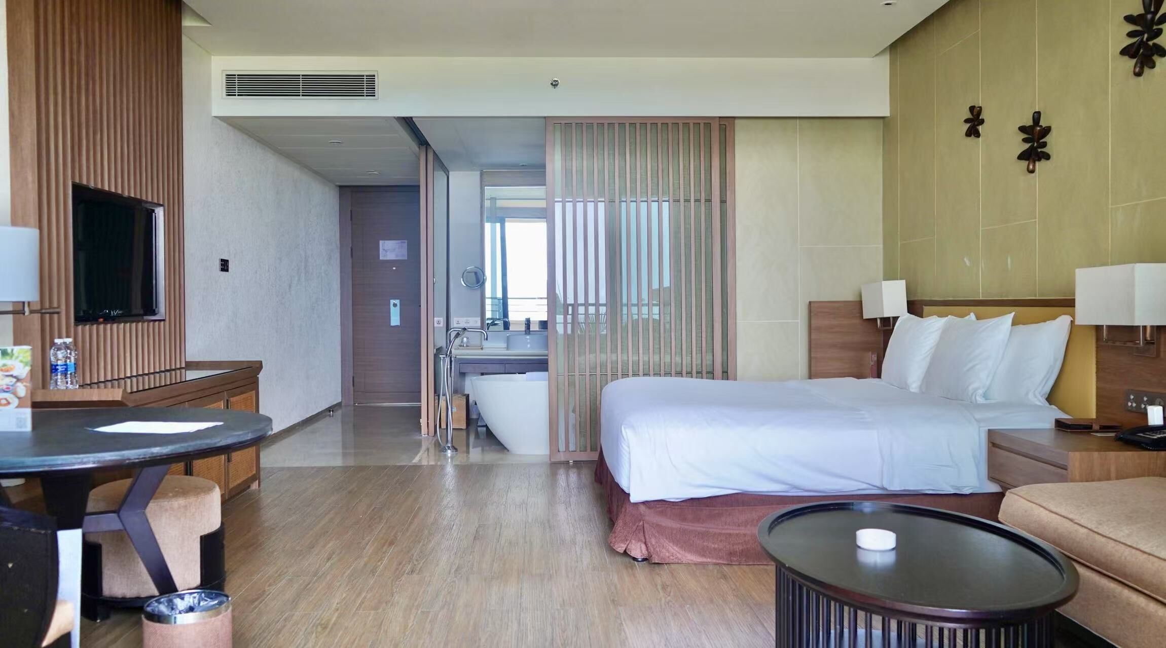 Habitación de hotel con cama, mesitas de noche, escritorio, televisor y baño visible a través de una puerta corredera.