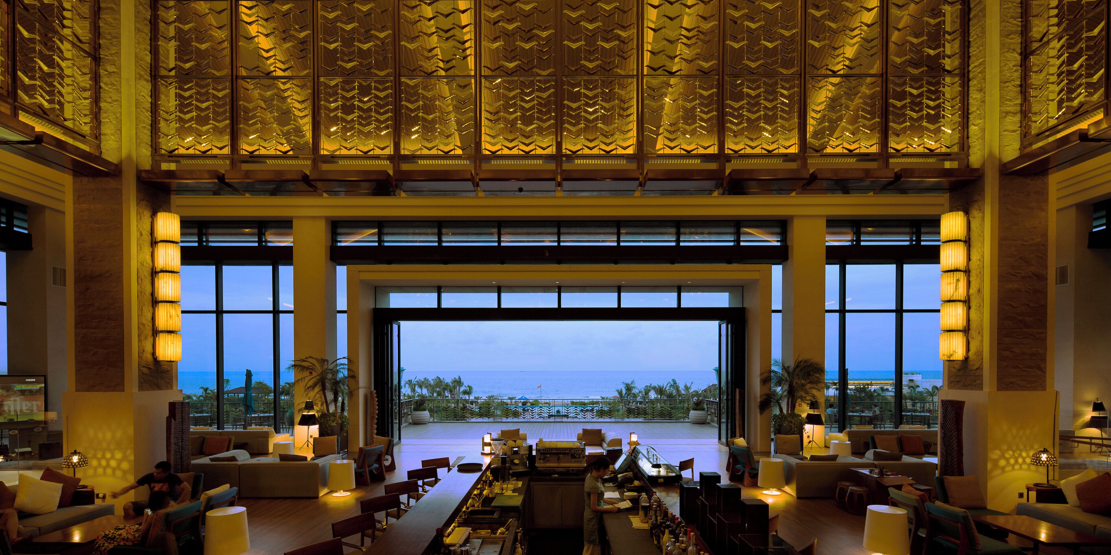 A spacious lobby with a large open doorway leading to a terrace with a view of the sea.
