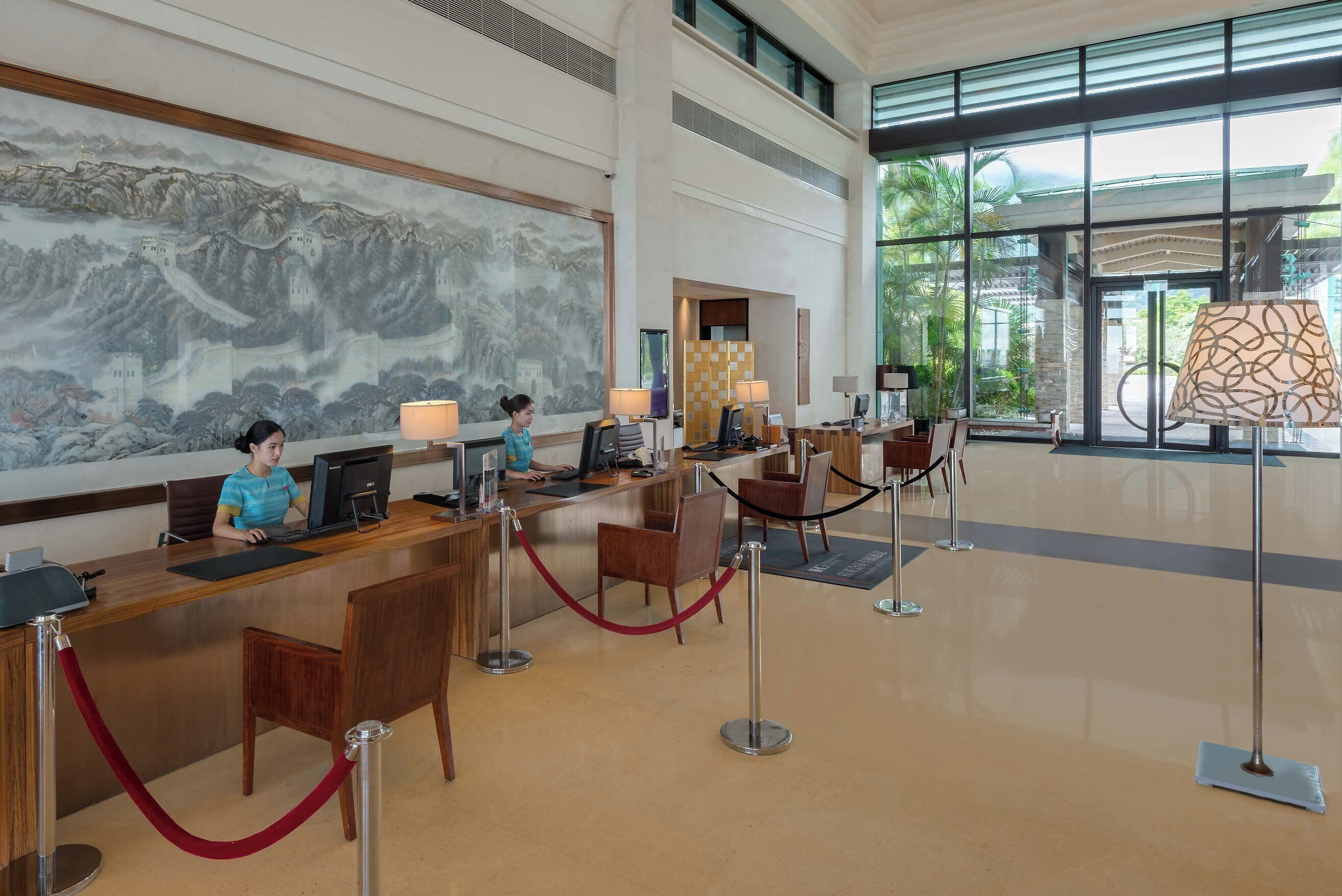 A reception area with a receptionist, computers, and a large window with a view of greenery.