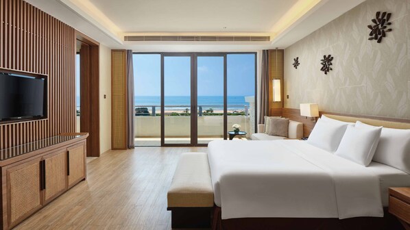 A hotel room with a large bed, a TV, and a balcony with a view of the beach.