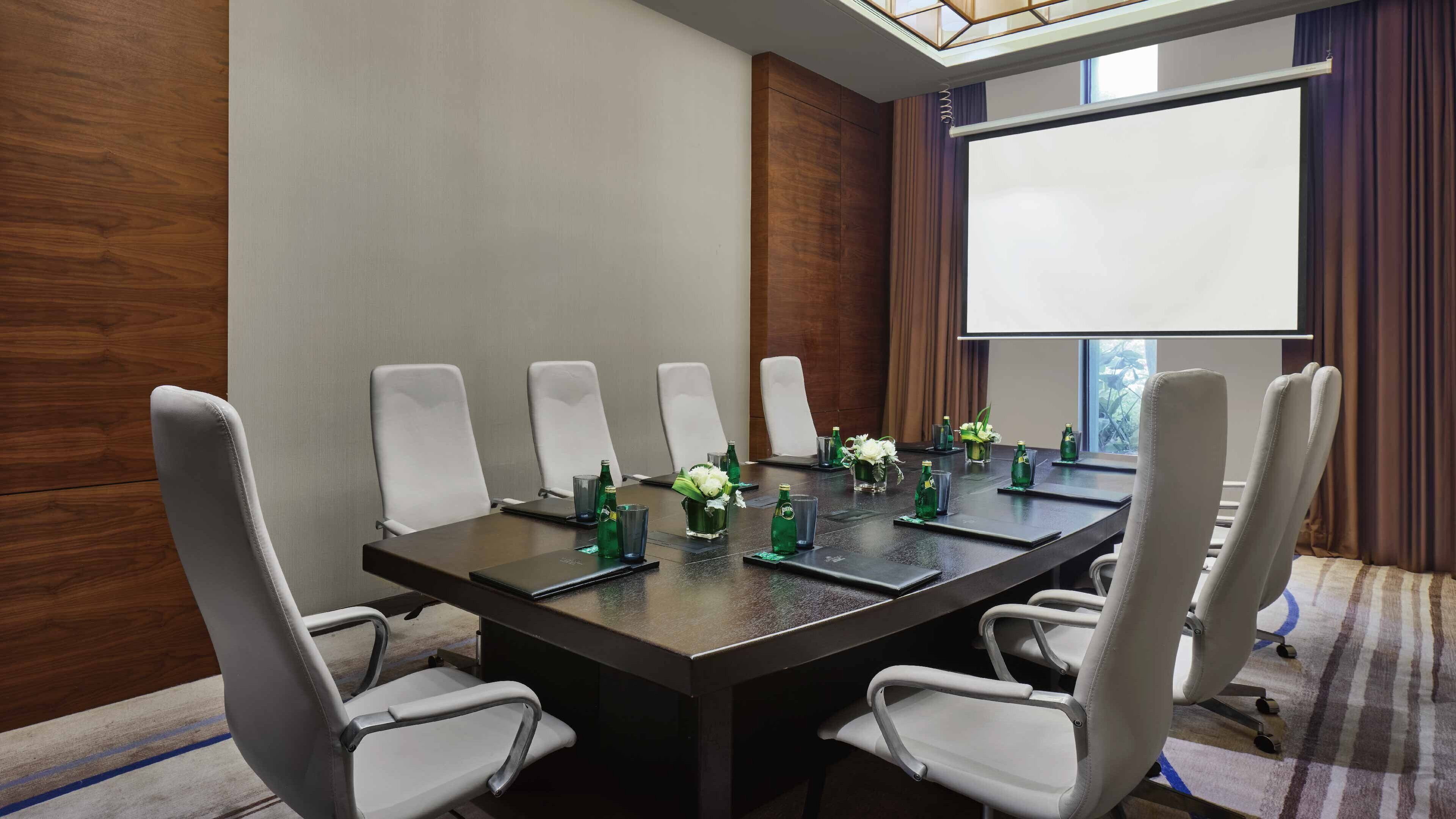 Une salle de conférence avec une longue table, six chaises blanches et un écran de projection.