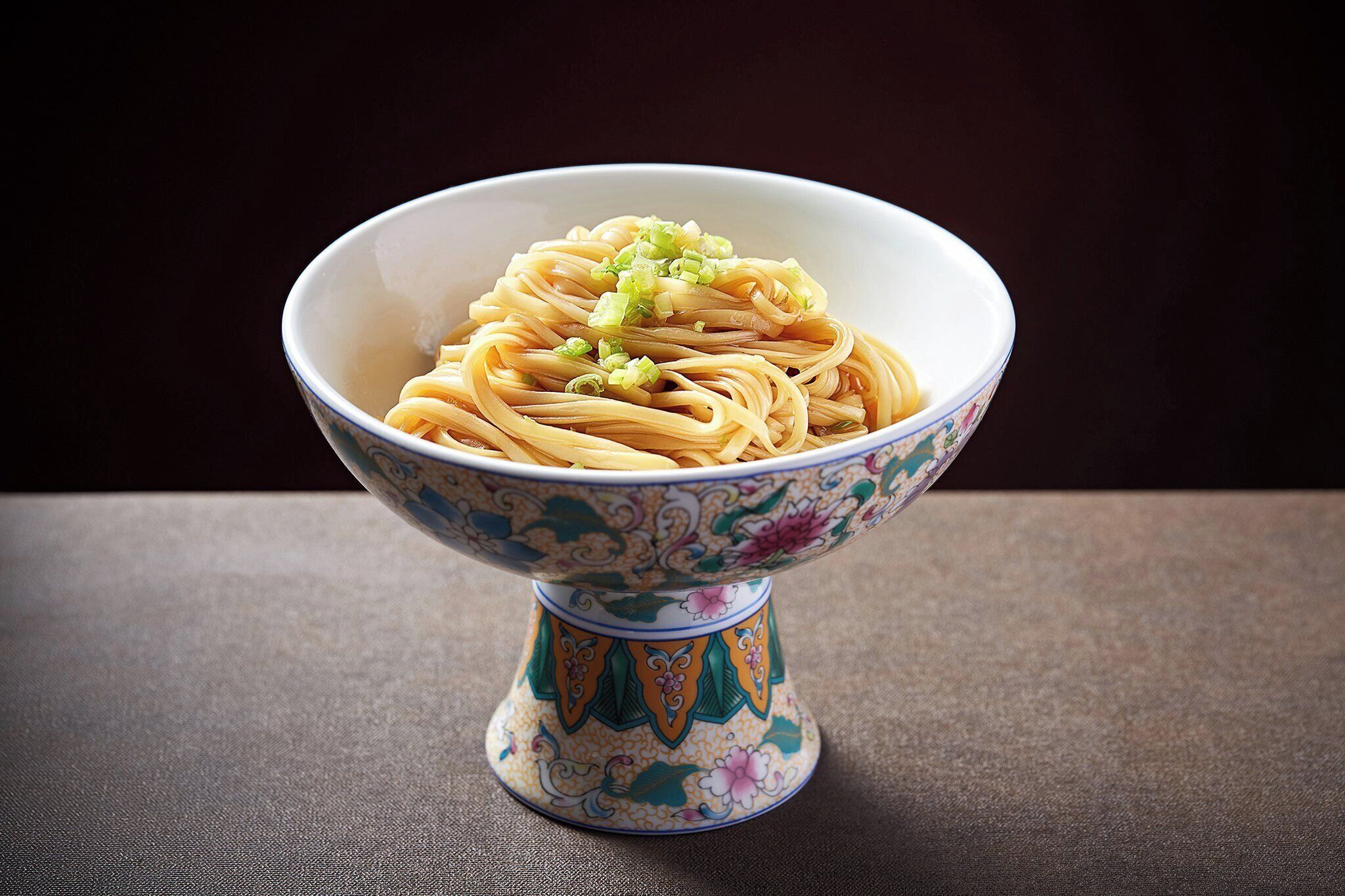 A bowl of noodles with green onions on a table.