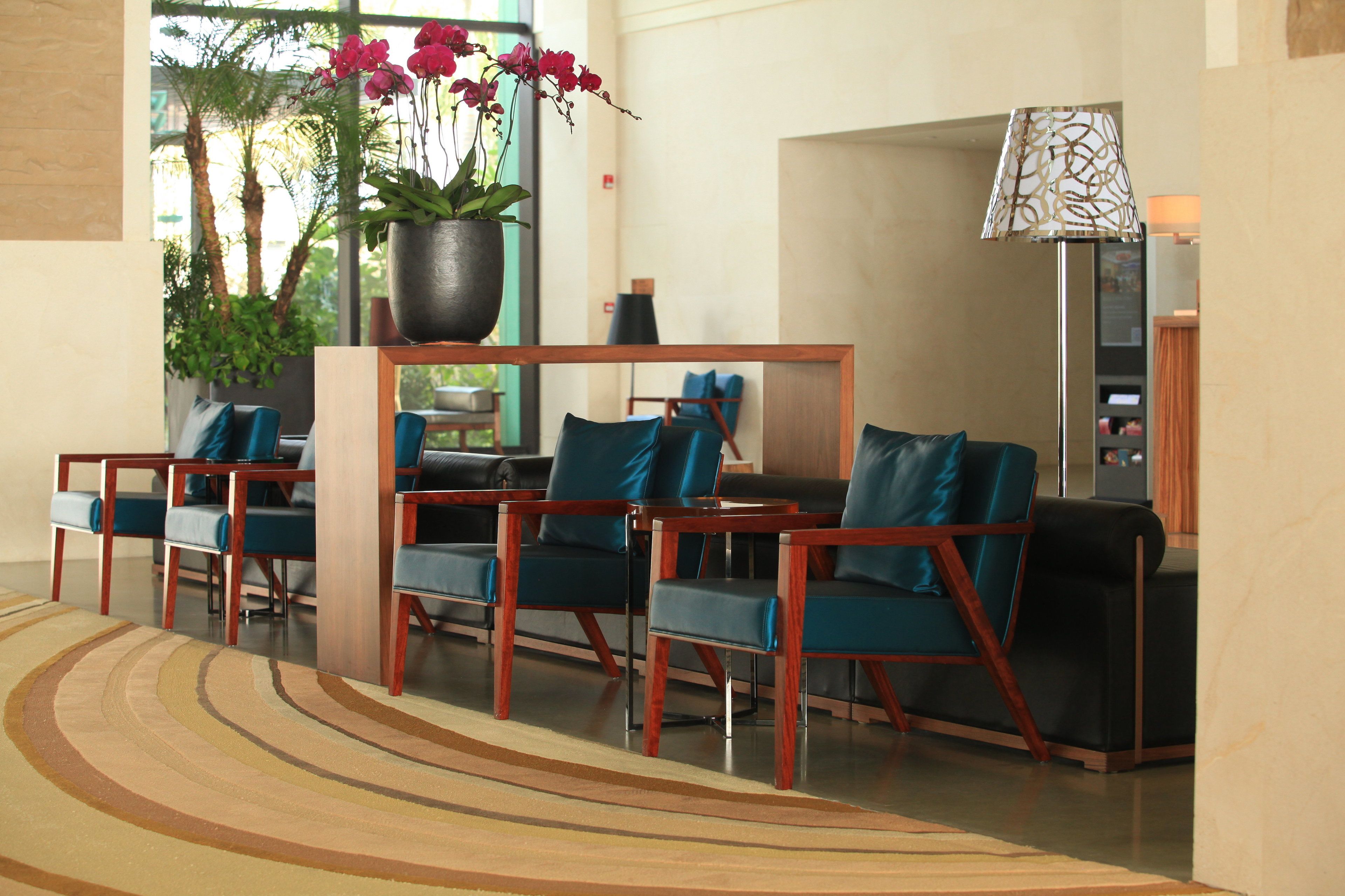 Un hall d’entrée avec un espace détente comprenant des chaises en bois et une table, une plante en pot ornée de fleurs et une lampe.