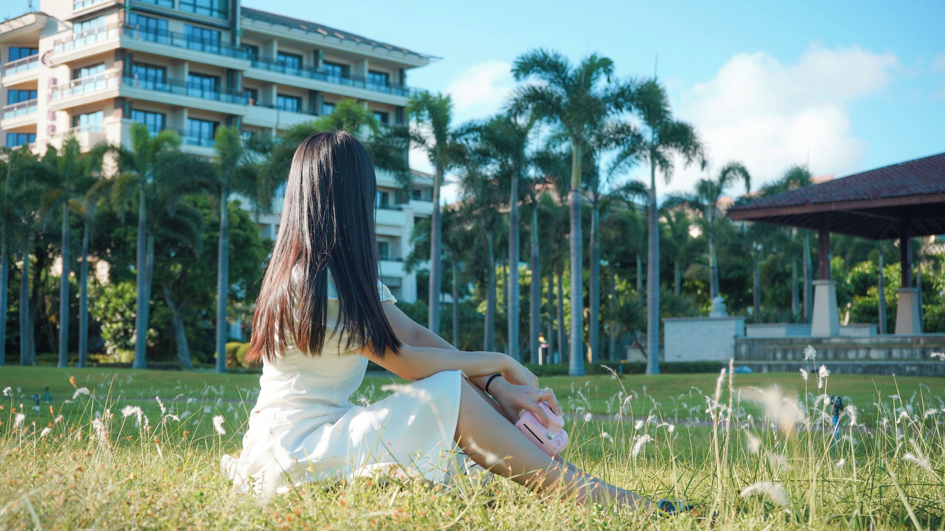 A person sitting on grass in a park with a building in the background.