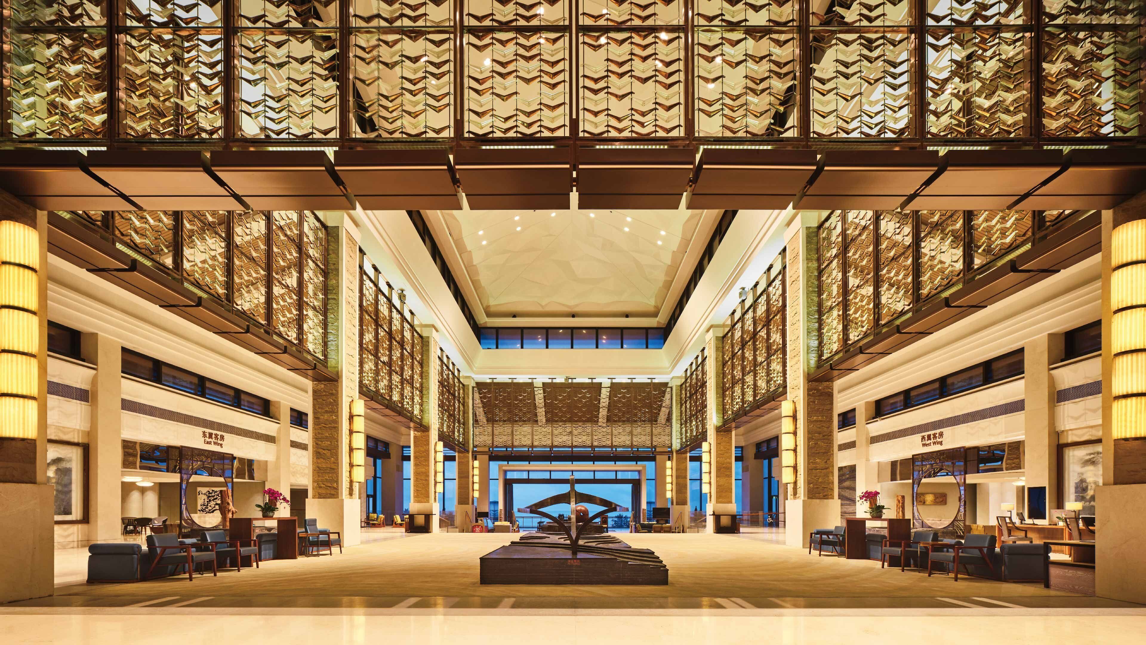 A spacious lobby with a central sculpture, high ceilings, and patterned glass windows.
