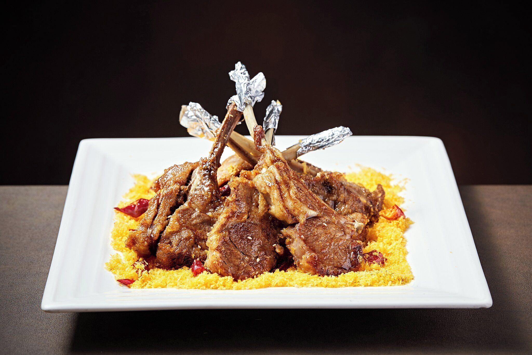 A white plate with grilled lamb chops on a bed of couscous.