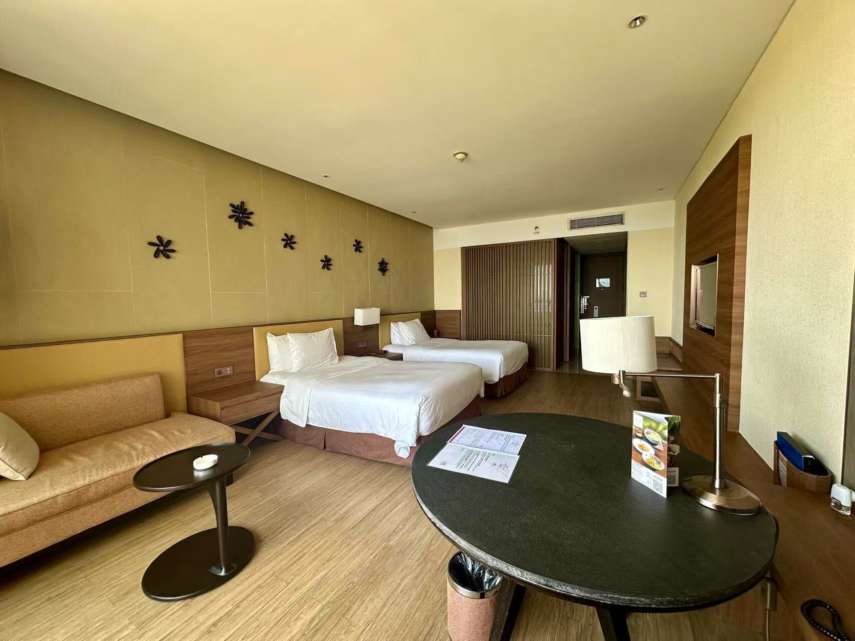 A hotel room with two beds, a sofa, a round table with a menu, and a trash bin.