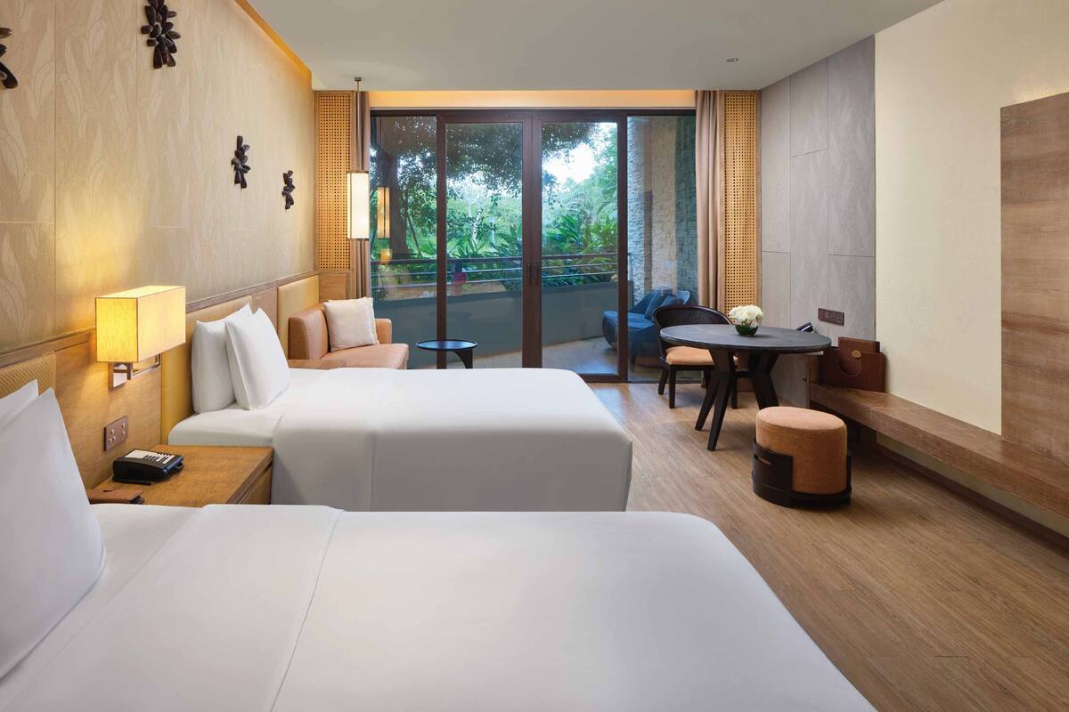 A hotel room with two beds, a small table, a chair, and a sofa.
