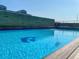 Una piscina con agua azul cristalina, un muelle de madera y un muro de ladrillo con una ventana.