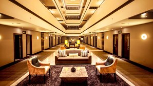 Un vestíbulo de hotel con una zona de estar central, varias puertas y un diseño de techo moderno.