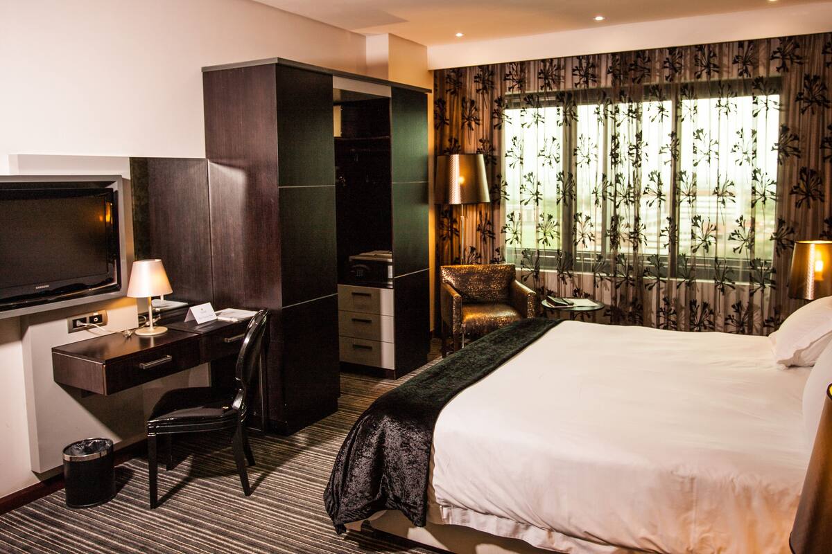 A hotel room with a bed, a desk, a chair, a TV, and a window with curtains.