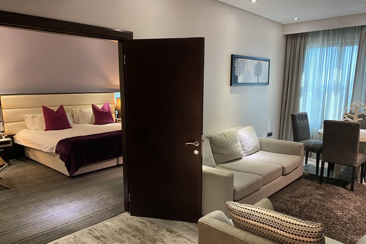 A hotel room with a bed, a sofa, a dining table, and a door.