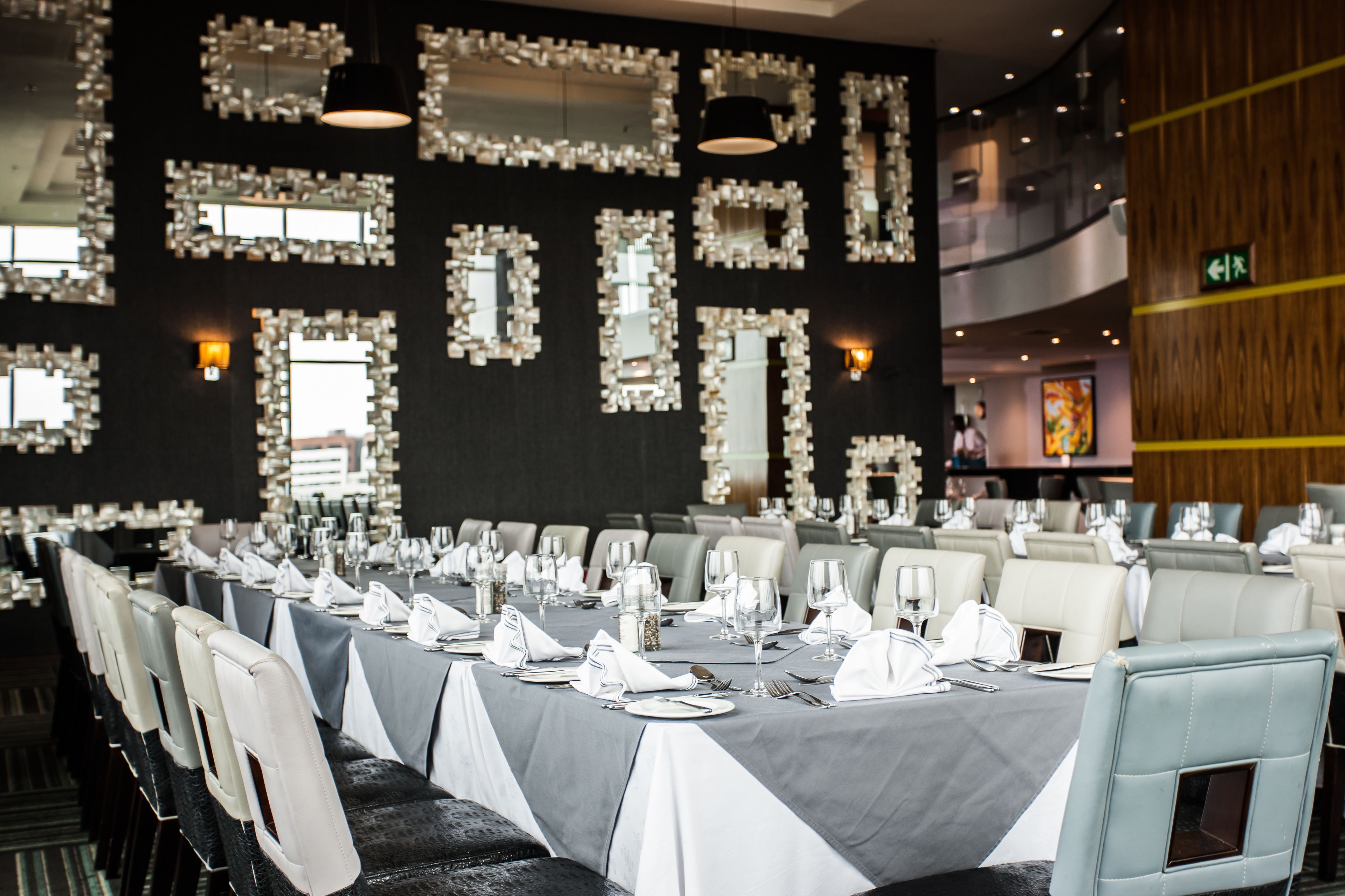 A long dining table set with white tablecloths, chairs, and fine china in a modern hotel dining area.