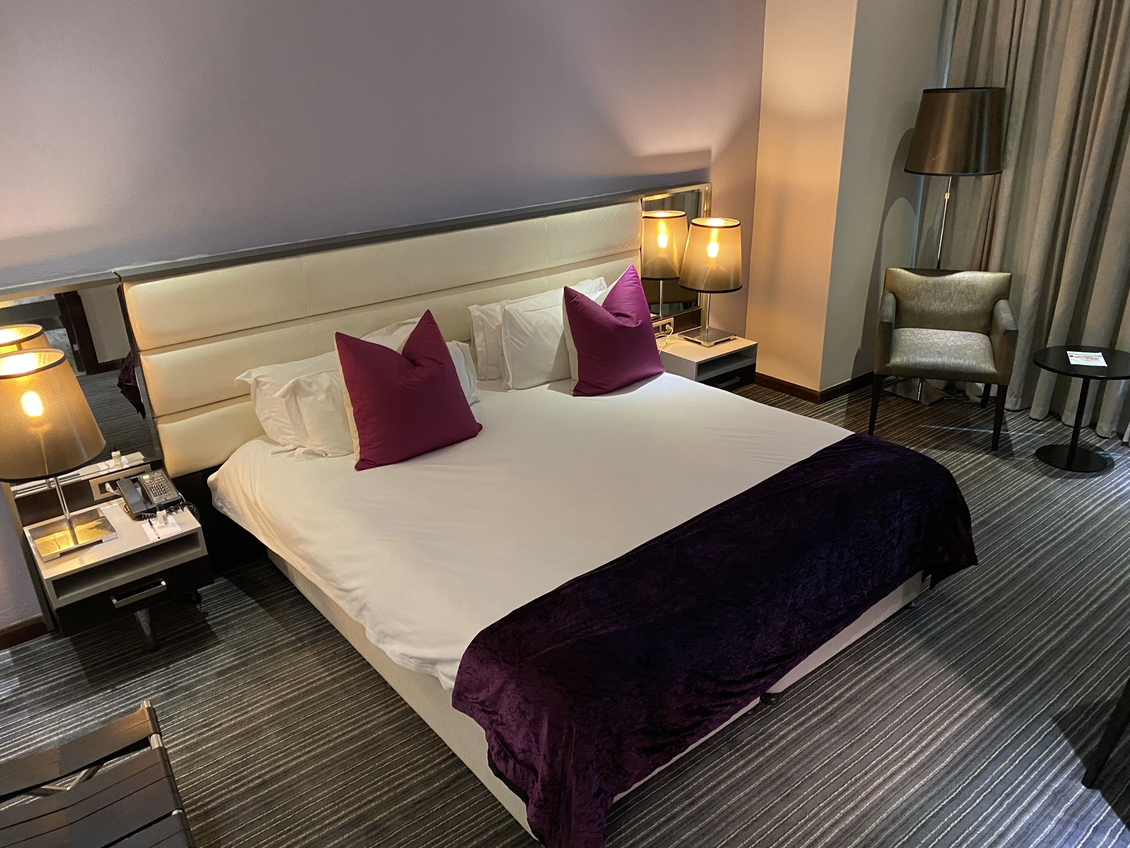 Una habitación de hotel con una cama grande, dos mesitas de noche con lámparas, una silla y un escritorio.