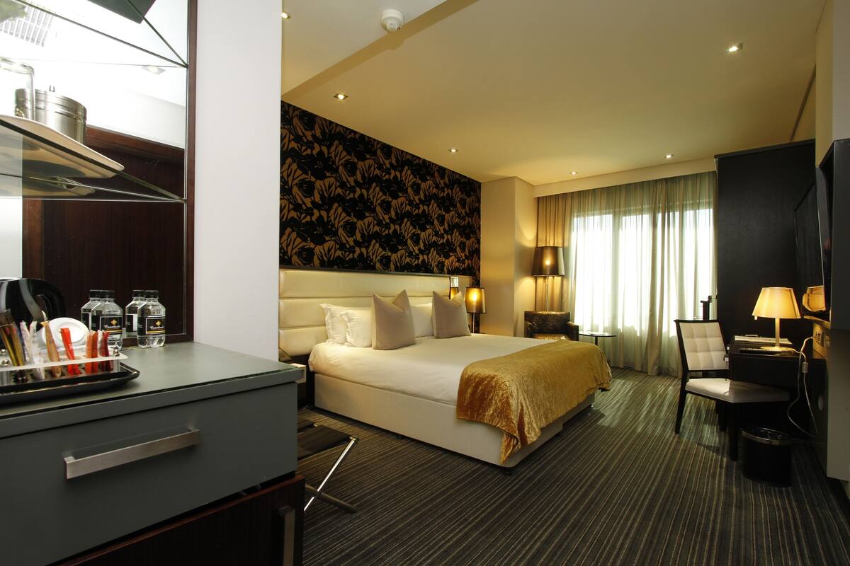 A hotel room with a large bed, a desk with a chair, a small table, and a lamp.