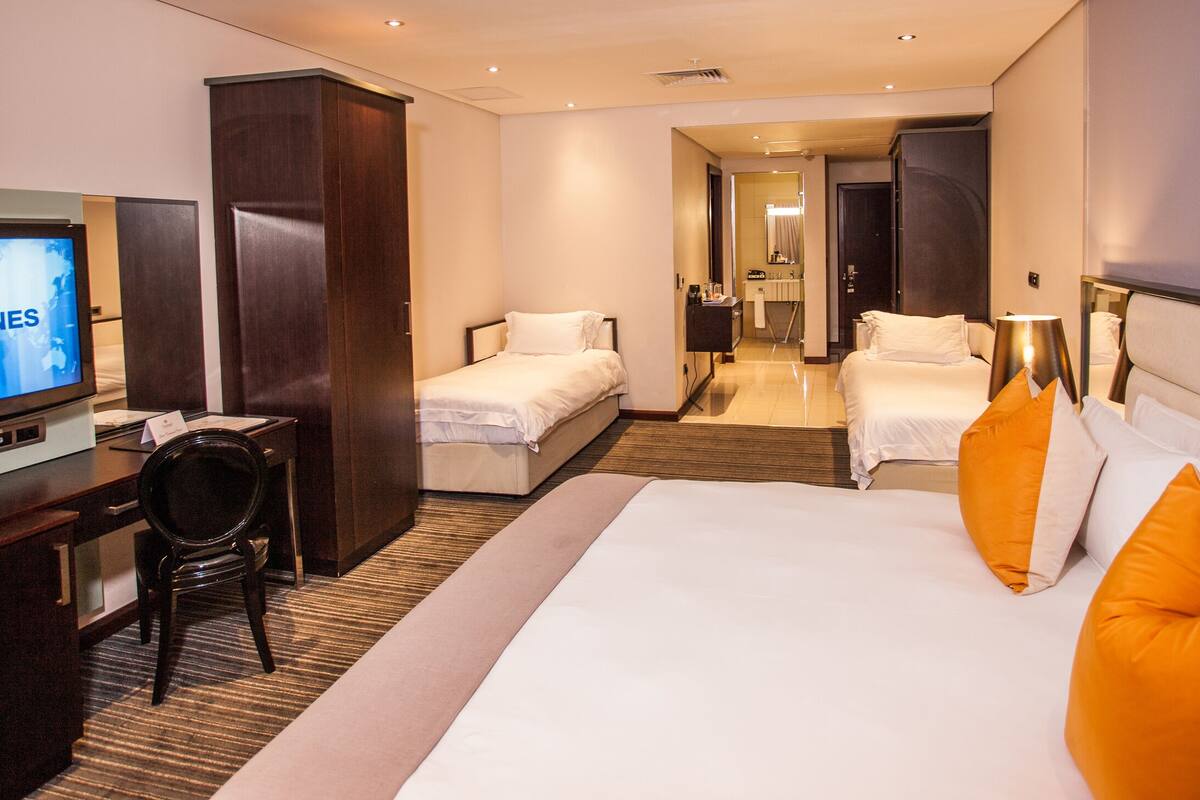 A hotel room with a bed, a desk with a television, a wardrobe, and a bathroom visible in the background.