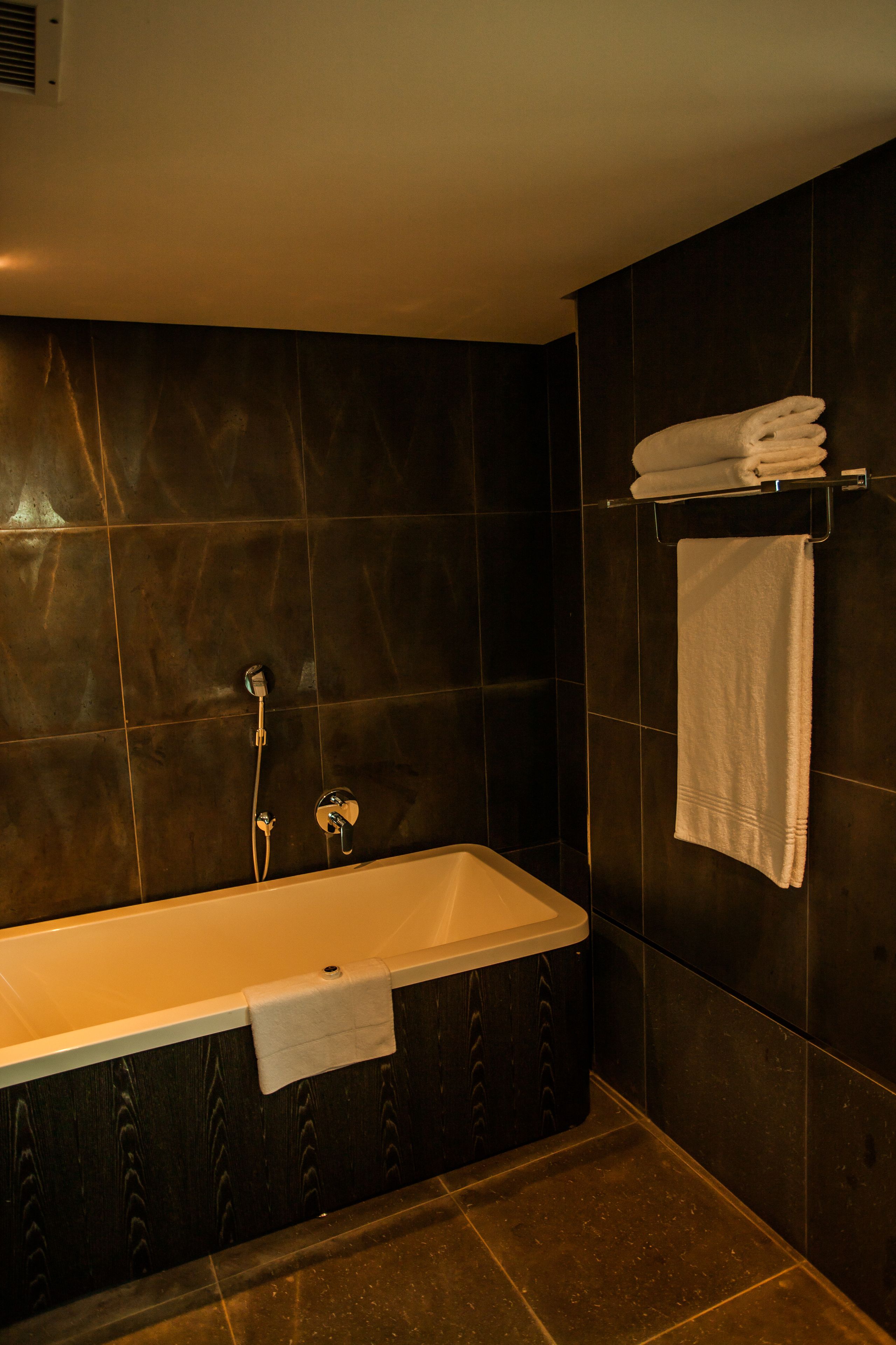 Une salle de bain moderne avec une baignoire sur pieds, des murs recouverts de carreaux foncés et un porte-serviettes avec des serviettes pliées.