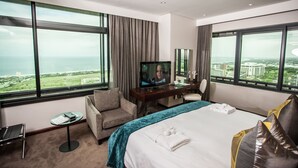Habitación de hotel con una cama grande, televisión, escritorio, silla y vistas a la ciudad y al mar.