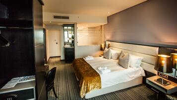 A hotel room with a large bed, a desk, a chair, and a minibar.