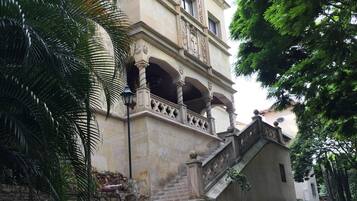 A building with a stone facade, a set of stairs leading to a balcony, and surrounding greenery.
