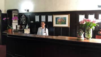 A reception desk with a receptionist, a framed picture, a vase with flowers, and a decorative item on the counter.