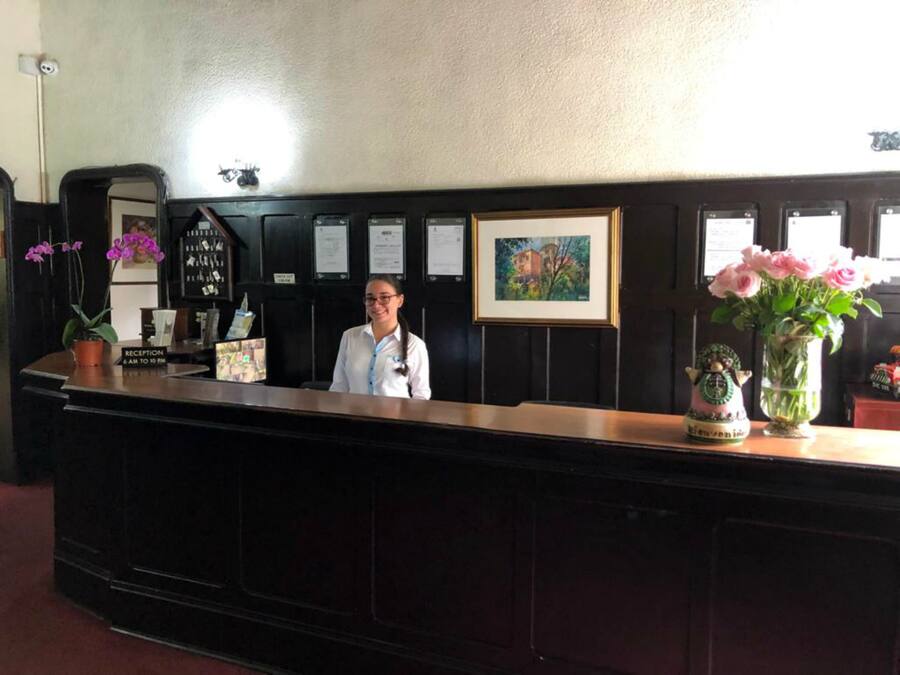 A reception desk with a receptionist, a framed picture, a vase with flowers, and a decorative item on the counter.