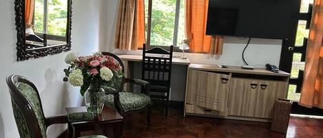 A room with a wooden herringbone floor, a dining table with chairs, a TV mounted on the wall, and a window with curtains.