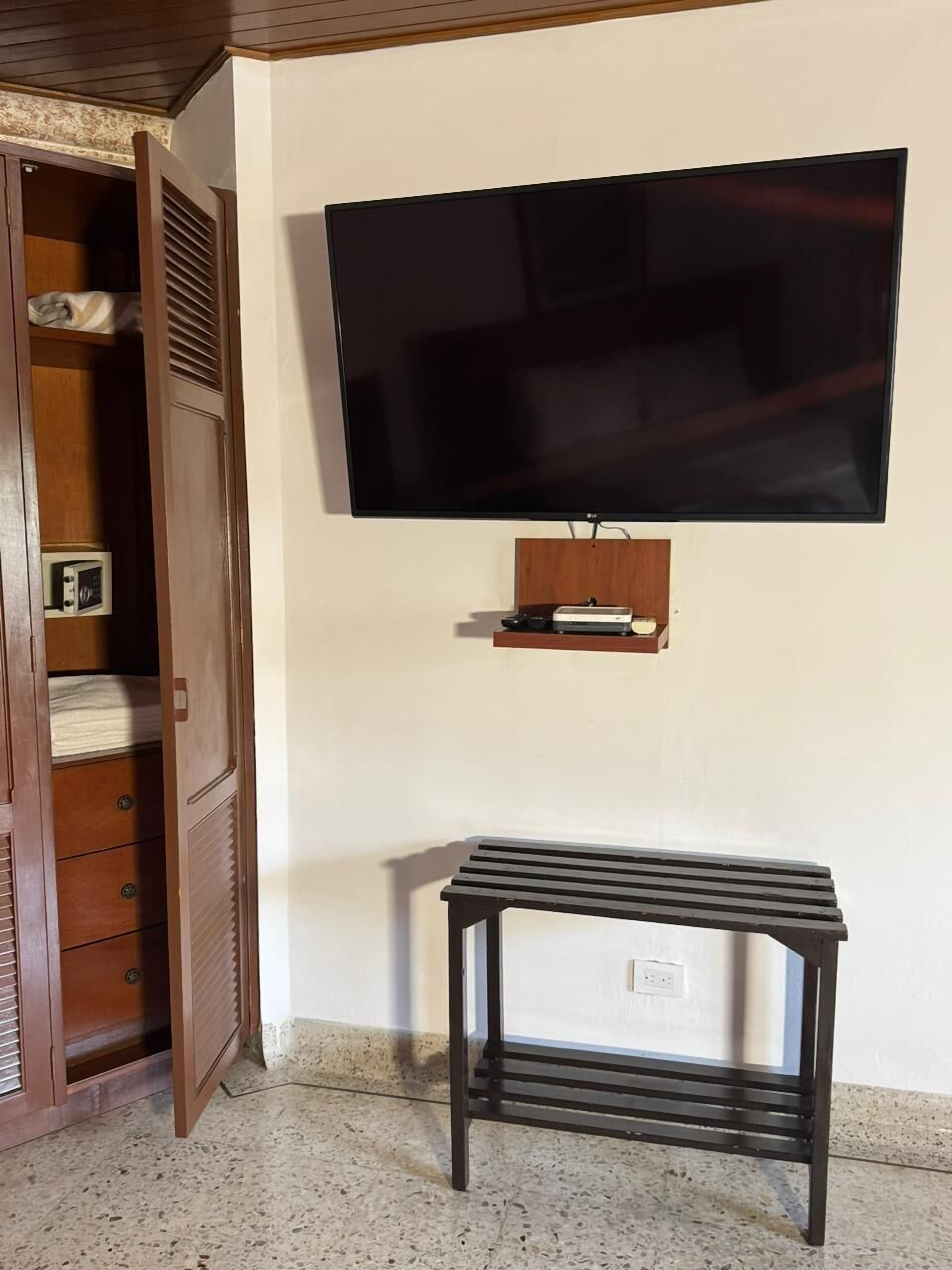 Una habitación con un armario de madera, un televisor montado en la pared y un pequeño estante debajo del televisor.