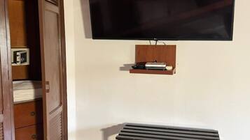 Una habitación con un armario de madera, un televisor montado en la pared y un pequeño estante debajo del televisor.