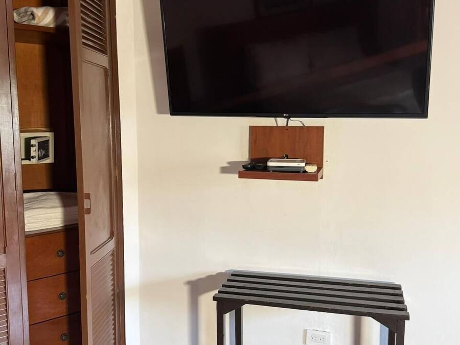 Una habitación con un armario de madera, un televisor montado en la pared y un pequeño estante debajo del televisor.