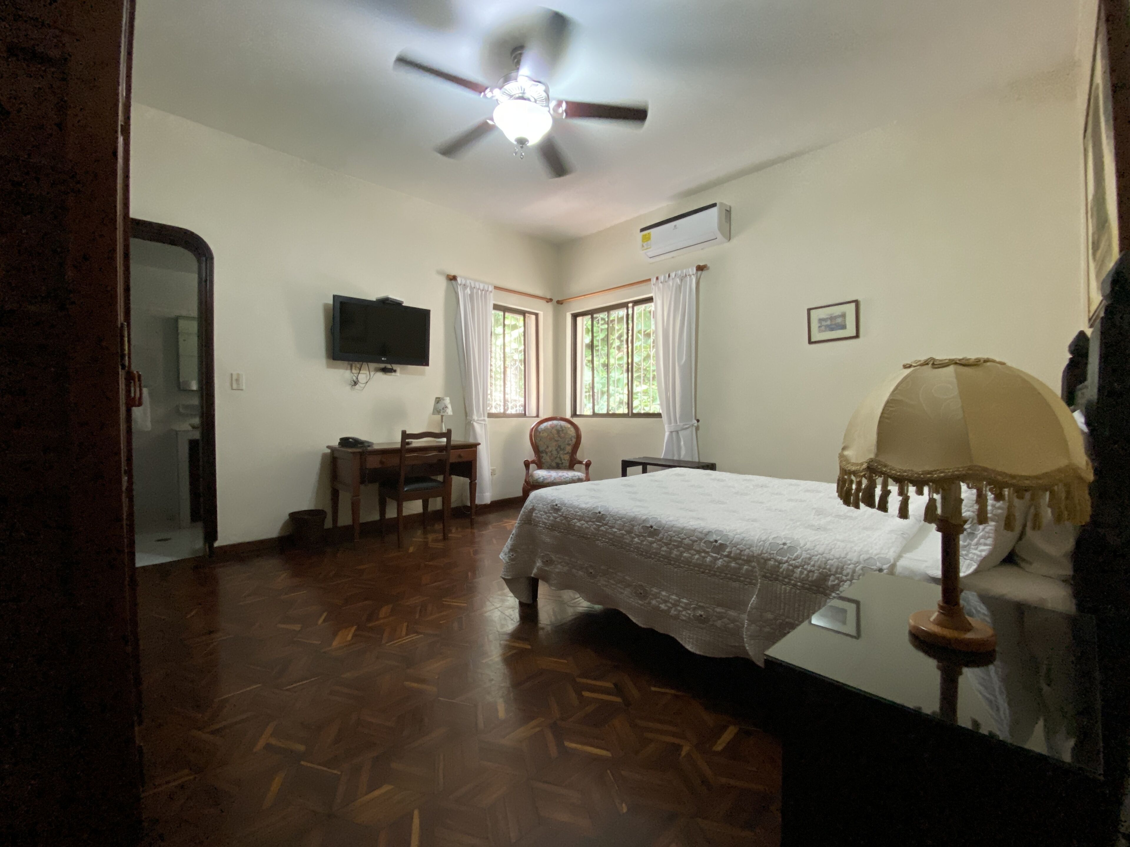 Ein Schlafzimmer mit Bett, Schreibtisch, Stuhl, Deckenventilator und Fernseher.
