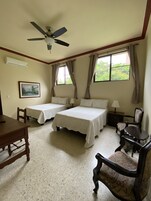 A hotel room with two beds, a desk, a chair, a ceiling fan, and a window with curtains.