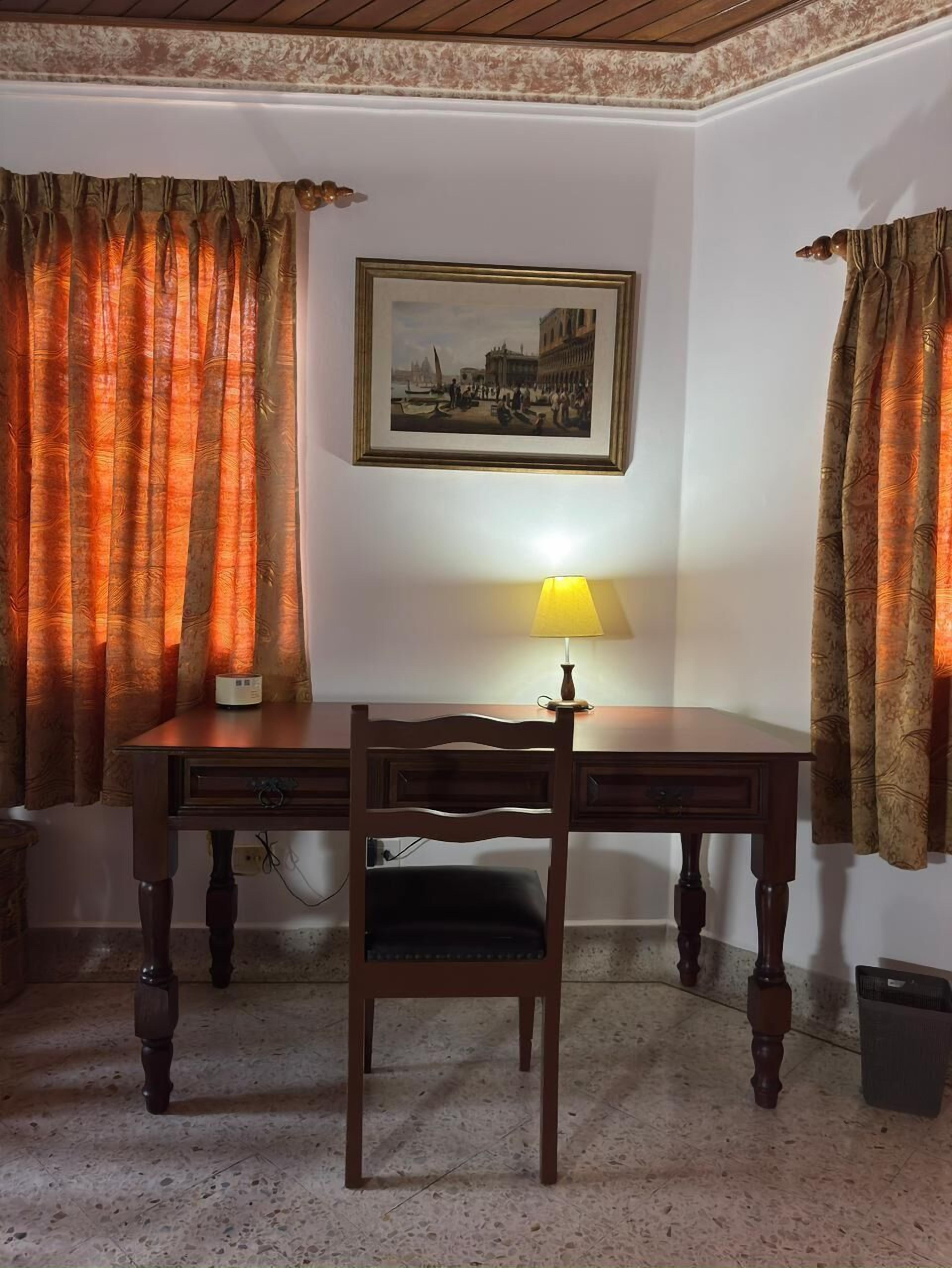 A room with a wooden desk, a chair, a lamp, and a framed picture on the wall.