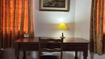 Una habitación con un escritorio de madera, una silla, una lámpara y un cuadro en la pared.