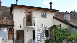 Uma casa de dois andares com uma escada em espiral, uma porta de madeira e uma pequena varanda.