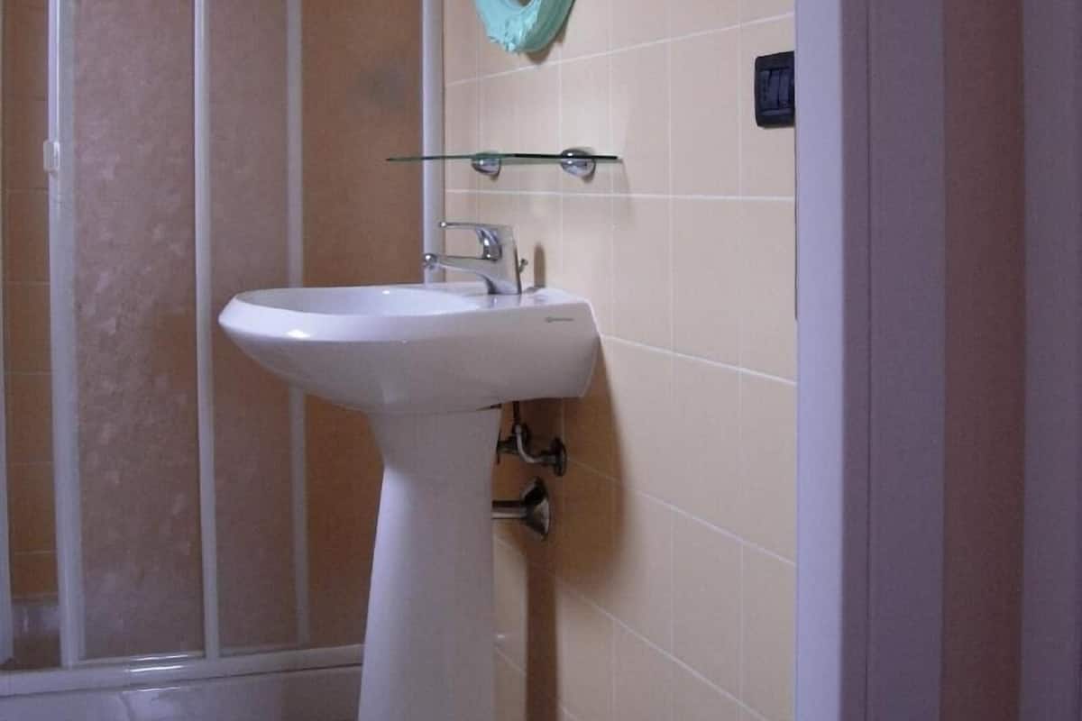 A bathroom with a pedestal sink, a mirror, and a shower enclosure.